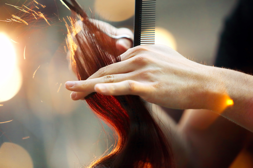 Close up of stylist cutting long, red hair.