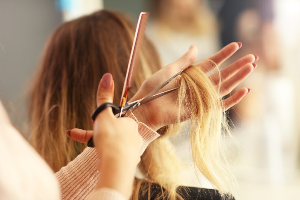 cosmetologist holding scissors and comb prepares to cut a length of hair