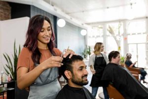 Student practicing haircut techniques at Austin Kade Academy salon w/ pro skin.