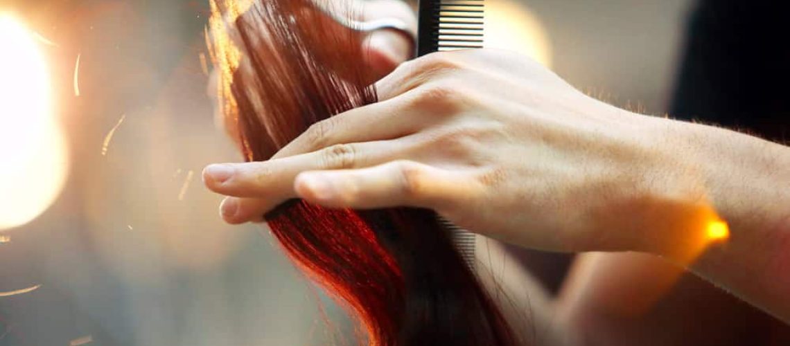 Close up of stylist cutting long, red hair.