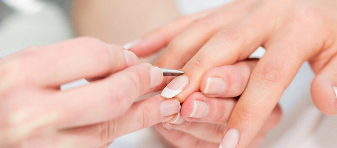 Esthetician performing nail care with a tool on a client's nails.