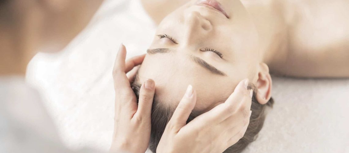 Esthetician performing facial massage on a woman in a spa setting.