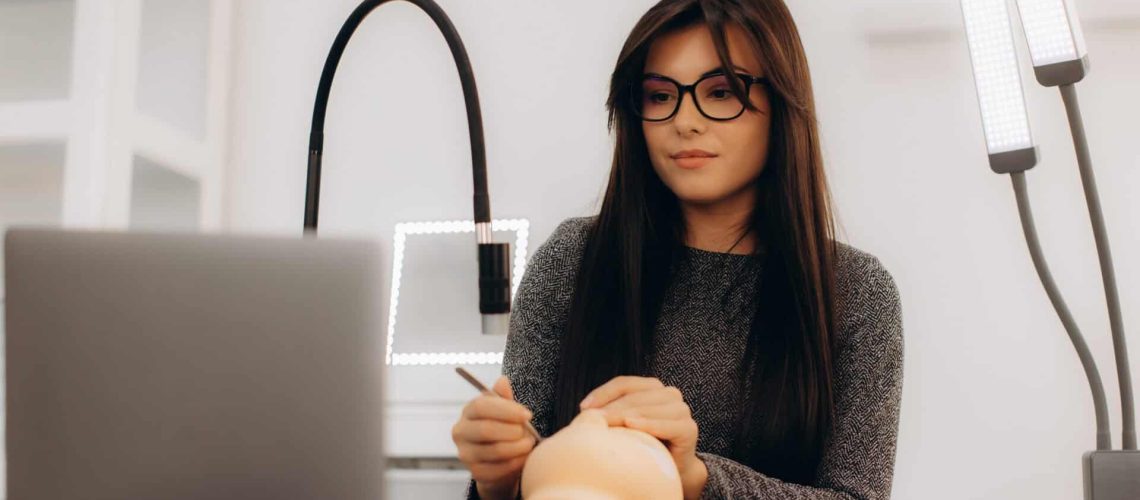 Young woman practicing cosmetology techniques with mannequin head in training lab.