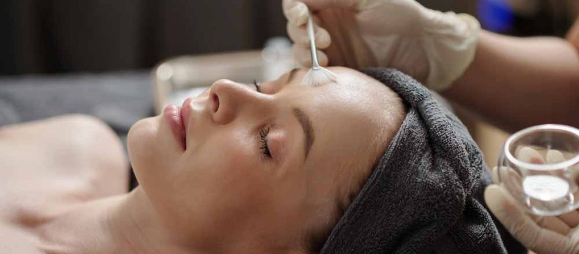 Esthetician applying glycolic acid peel on face of young woman